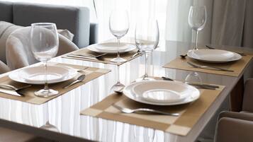 Een eettafel gedekt met borden, bestek en wijnglazen, met een bankstel op de achtergrond.