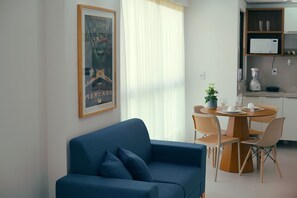 A modern living room with a blue sofa, a dining area with a round table and chairs, a kitchen with a microwave and a blender, and a framed picture on the wall. - Botanik With Coworking, Pet Place, and Skyview By Carpediem (Recife)