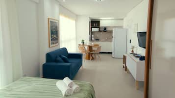 Een knus hotelkamer met een bed, een blauwe slaapbank, een eettafel met stoelen, een kitchenette en een televisie.