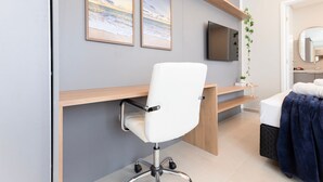 Ein modernes Zimmer mit weißem Bürostuhl, einem an der Wand montierten Fernseher und einem Bett mit blauer Decke.
