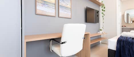 Una habitación moderna con una silla de escritorio blanca, un televisor montado en la pared y una cama con una colcha azul.