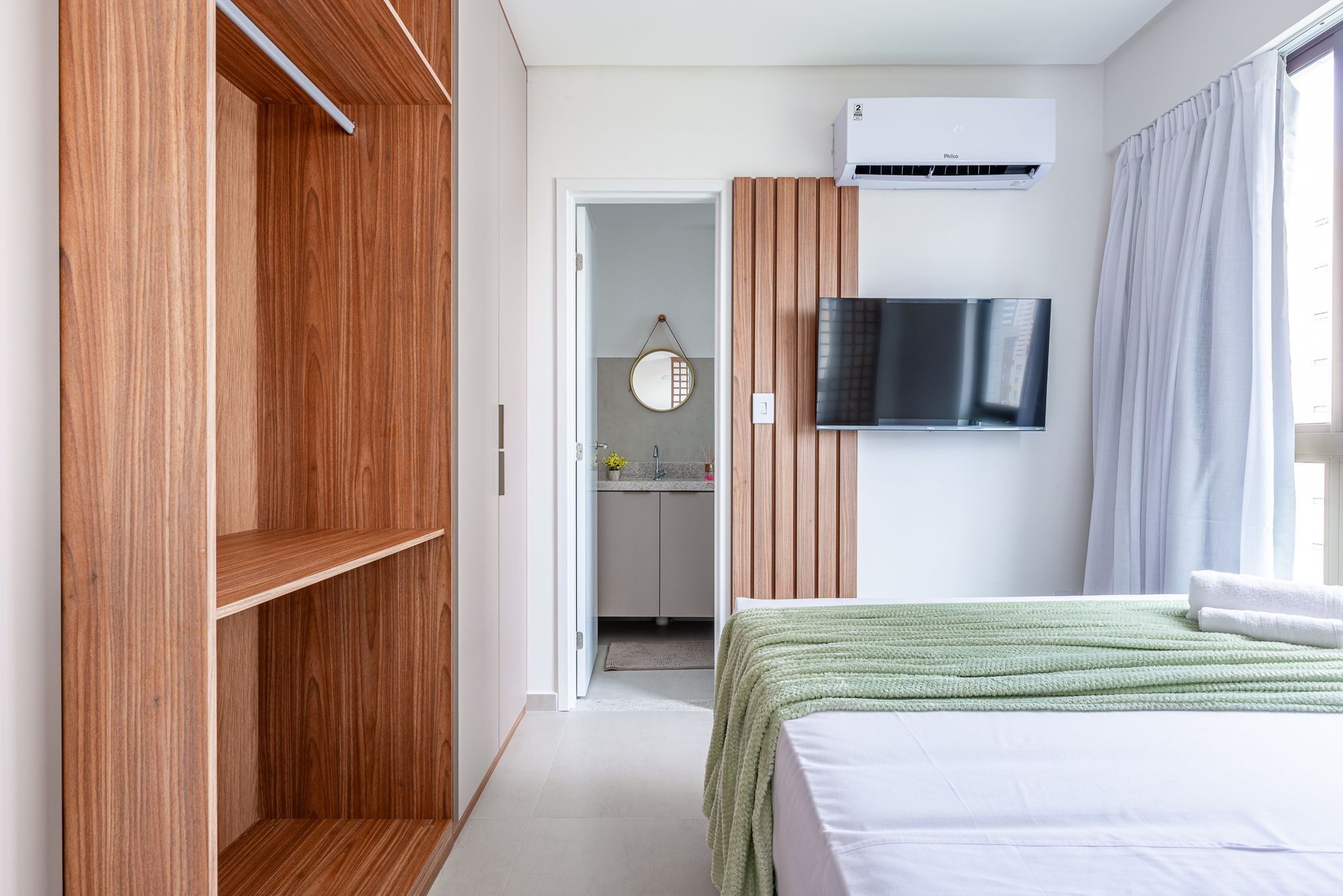 Quarto de hotel com guarda-roupa, televisão, cama e casa de banho visível através de uma porta aberta.