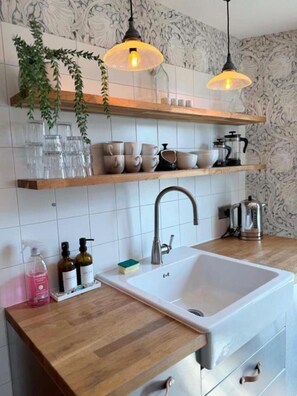 A kitchen with wooden countertops, a white sink, hanging pendant lights, and shelves with glassware and kitchenware. - Poppy's Studio Collection - Harbour Townhouse and The Hideaway (Mevagissey)