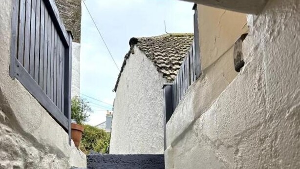 Una escalera estrecha con paredes blancas y escalones oscuros que conducen a un tejado de azulejos.