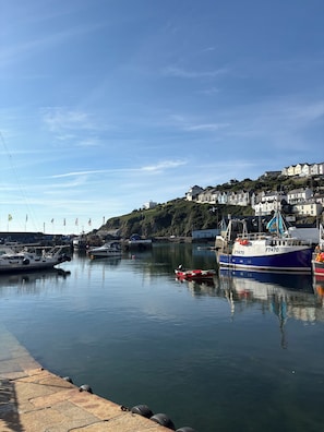 Un port avec des bateaux, un quai et des bâtiments situés sur le versant d’une colline.