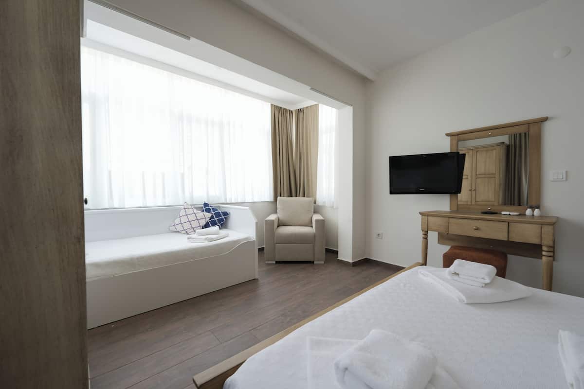 Hotellihuone, jossa on sänky, sohva, tuoli, televisio, työpöytä ja ikkuna, jossa on verhot.