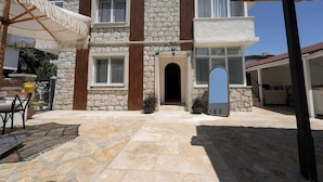 Un edificio de piedra de dos pisos con entrada central, un área de estar al aire libre cubierta y un espejo grande.