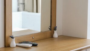 Un aparador de madera con un espejo, un florero y un control remoto.
