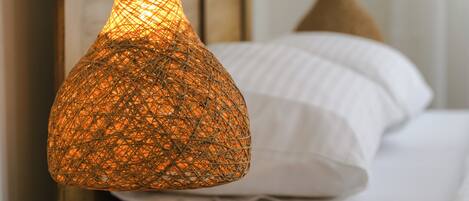 A bed with white linens, a wooden headboard, and a hanging woven light fixture.
