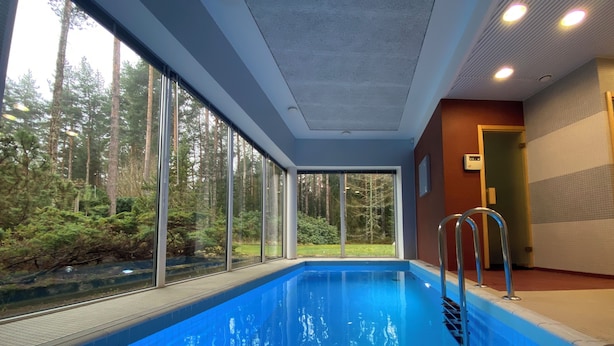 Ein Hallenbad mit großen Glaswänden, einer Metallleiter und Blick auf eine bewaldete Landschaft.