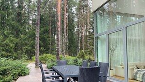 Ein moderner Essbereich im Freien mit Tisch und Stühlen, umgeben von einer Holzterrasse und dichtem Wald.