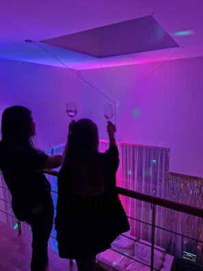 Deux personnes tenant des verres à vin dans une pièce dotée d’un plafond au design moderne et offrant une vue sur un bâtiment à l’extérieur.