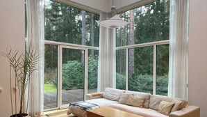 Ein modernes Wohnzimmer mit einer Couch, einem Holztisch und großen Fenstern mit Blick auf einen Wald.