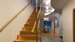 Eine moderne Treppe mit Holzstufen und Metallgeländern, die zu einem Essbereich mit Blick auf Bäume führt.