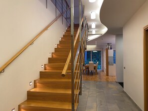 A modern staircase with wooden steps and metal railings, leading to a dining area with a view of trees.