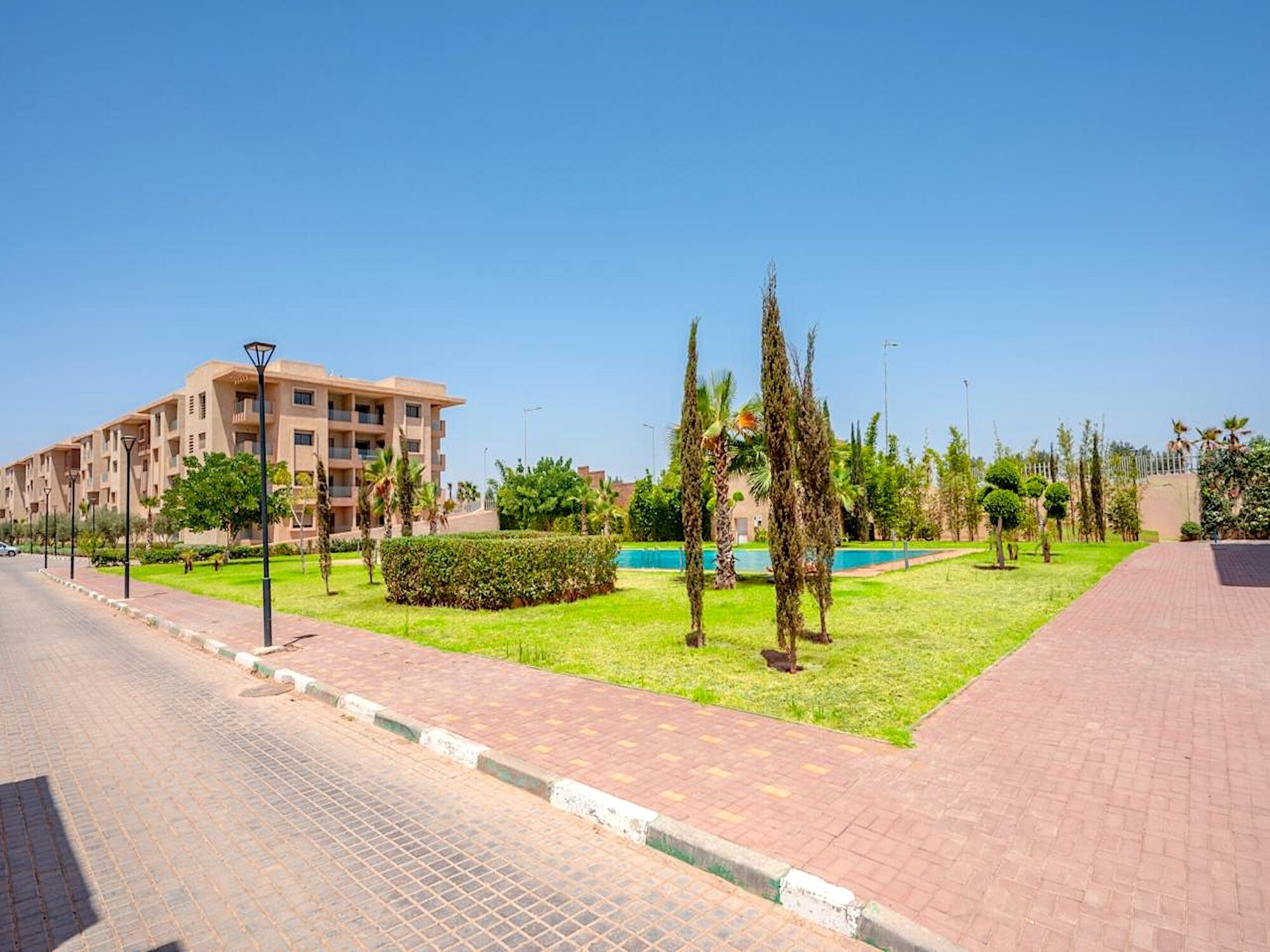 A residential building with a paved walkway, a well-maintained lawn, and a pool.
