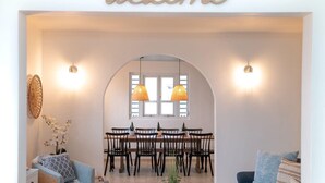 Zona pranzo con un cartello che riporta la scritta 'welcome', sedie di legno, un tavolo e due lampade a sospensione.