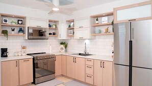 Una cucina moderna con mobili chiari in legno, un frigorifero in acciaio inossidabile, forno integrato e una ventola a soffitto.