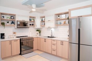 Eine moderne Küche mit hellen Holzschränken, einem Edelstahlkühlschrank, einem eingebauten Backofen und einem Deckenventilator.