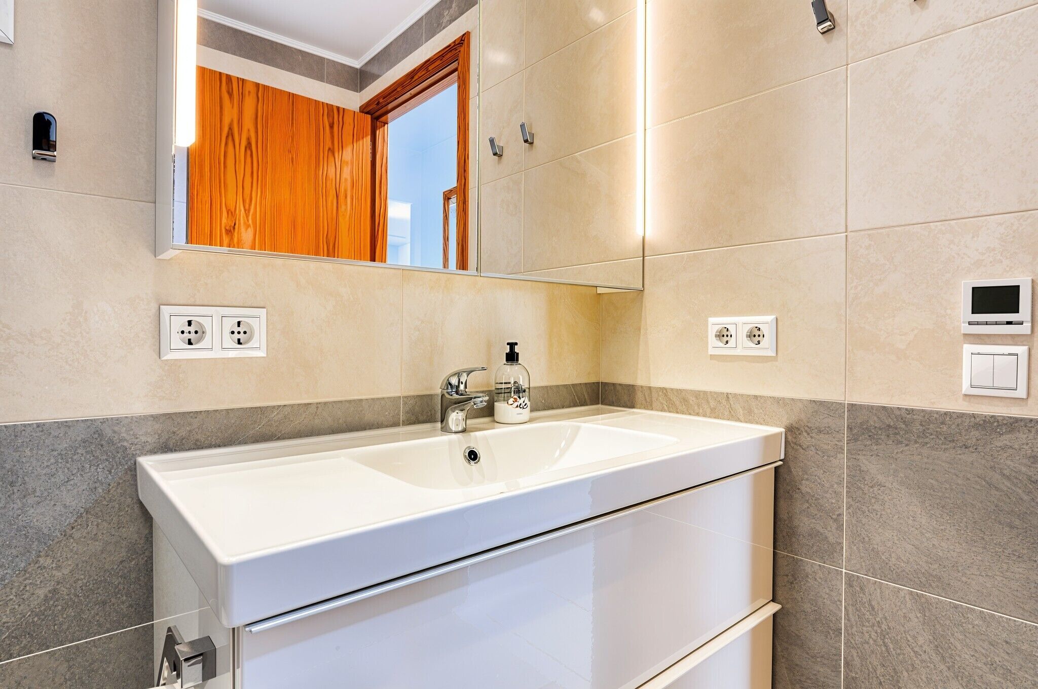 A bathroom with a double sink, a mirror, and a wooden door.