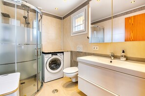 Een moderne badkamer met een douchecabine, een wasmachine, een toilet en een grote spiegel.