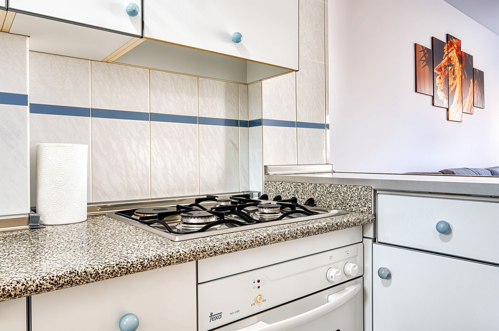 A kitchen with a gas stove, white cabinets, and a blue stripe on the wall.