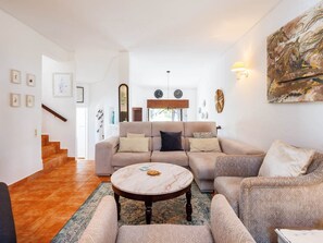 Ein Wohnzimmer mit einer Couch, Sesseln, einem Couchtisch und einer Treppe, die in einen anderen Raum führt.