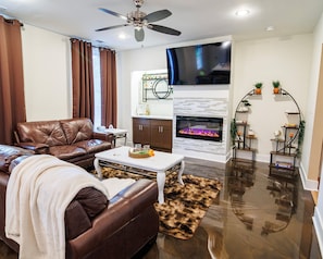 Ein Wohnzimmer mit braunem Ledersofa, einem weißen Couchtisch, einem Kamin und einem Deckenventilator.