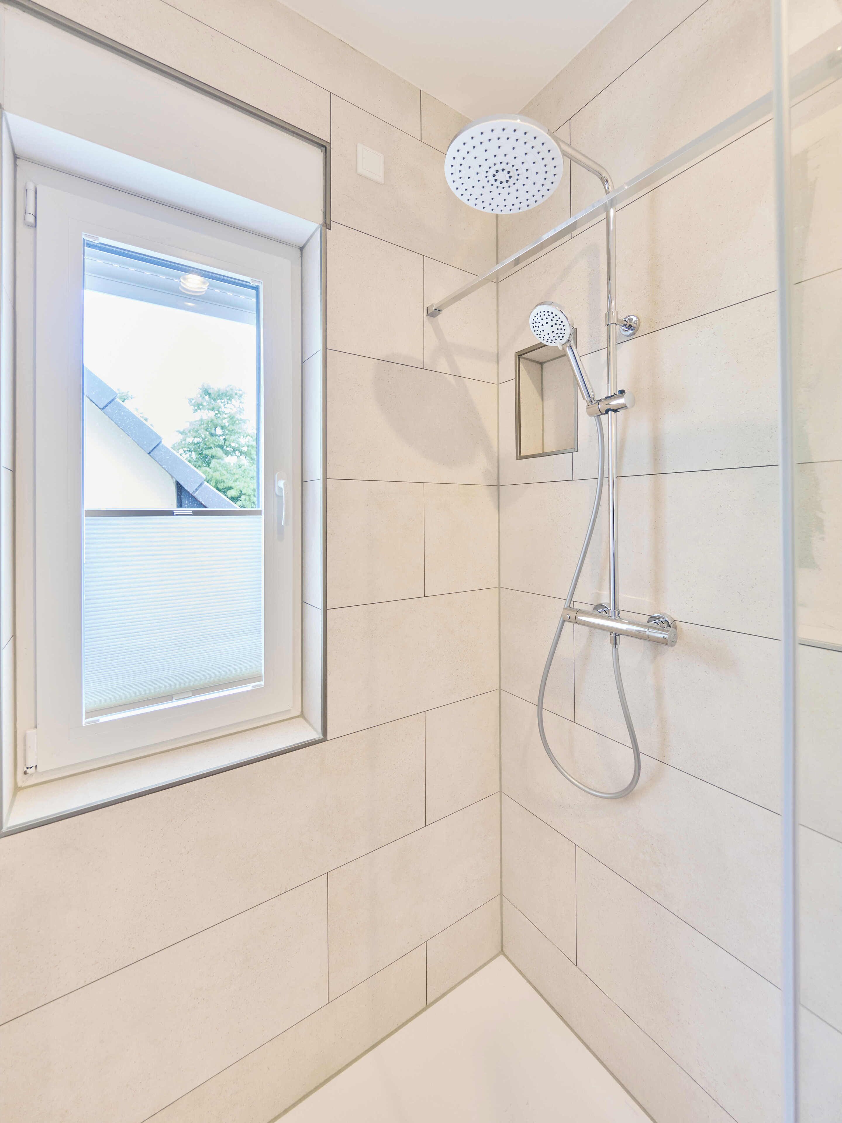 Eine Dusche mit Duschbrause, einer fest installierten Bedienfeld und einem Fenster mit Jalousien.