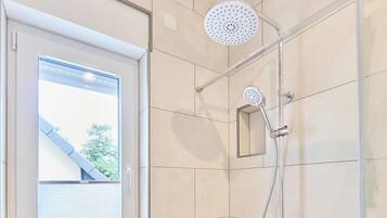 Eine Dusche mit Duschbrause, einer fest installierten Bedienfeld und einem Fenster mit Jalousien.