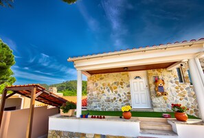 Una casa de piedra con un porche, una puerta blanca y un adorno de osito de peluche.