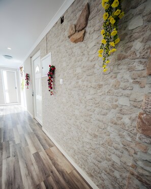 Un pasillo con pared de piedra, suelo de madera y arreglos florales colgantes.