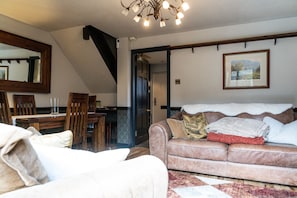 Een woonkamer met een bank, een eettafel, stoelen, een kroonluchter en een schilderij aan de muur.
