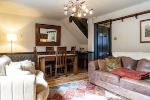 Een woonkamer met een bank, een eettafel met stoelen, een kroonluchter en een trap.