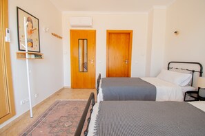 A room with two beds, a wooden door, a framed picture on the wall, and a standing heater. - Casa Cardhu in Carvoeiro (Lagoa)