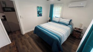Une chambre à coucher avec un lit, un ventilateur de plafond, un climatiseur, une table de chevet et un tableau au mur.