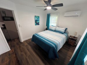 Ein Schlafzimmer mit Bett, Deckenventilator, Klimaanlage, Nachttisch und einem Bild an der Wand.