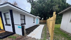 Une maison de plain-pied avec une façade blanche, une porte bleue et une clôture en bois.
