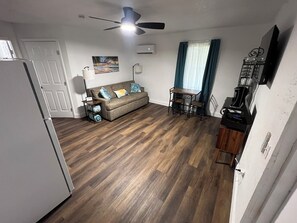 Ein kompakter Wohnbereich mit Küchenzeile, einer Couch mit Zierkissen, einem Esstisch mit Stühlen und einem Deckenventilator.