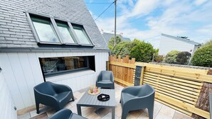 Eine Terrasse mit Tisch und vier Stühlen, ein Holzzaun und ein Gebäude mit Satteldach.