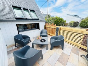 A patio with a table and four chairs, a wooden fence, and a building with a sloped roof.