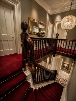 Una gran escalera con alfombra roja, barandilla de madera y un candelabro.