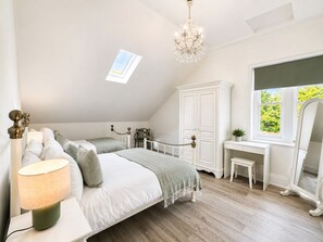 Une chambre Ă coucher comprenant un lit, une table de chevet, une lampe, une commode, un miroir et une fenĂȘtre donnant sur un paysage verdoyant.