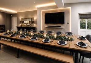 Une longue table à manger, dressée pour un repas formel, agrémentée de bougies et de verdure.