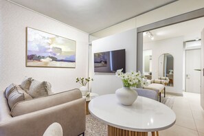 Ein modernes Wohnzimmer mit einem beigefarbenen Sofa, einem runden weißen Tisch mit Blumen und Bildern an den Wänden.