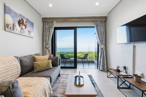 A modern living room with a sofa, a coffee table, a TV, and a balcony with a view. - Coastal Luxe | Umhlanga 1x BED Ocean Views (Umhlanga)