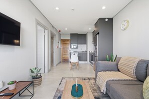 Ein modernes Wohnzimmer mit einer Couch, einem Couchtisch, einem Fernseher und einer Küche im Hintergrund.