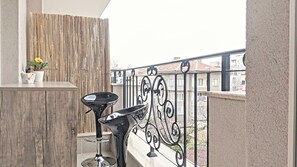 Ein Balkon mit Bambuswand, einer Topfpflanze, einer Vogelstatue und einem schwarzen Metallstuhl.