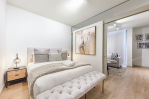 Ein modernes Schlafzimmer mit Bett, Nachttisch, Bank und Kunstwerk.