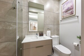 Ein modernes Badezimmer mit einer Duschkabine aus Glas, einem weißen Waschbecken, einer Toilette und einem gerahmten abstrakten Gemälde an der Wand.